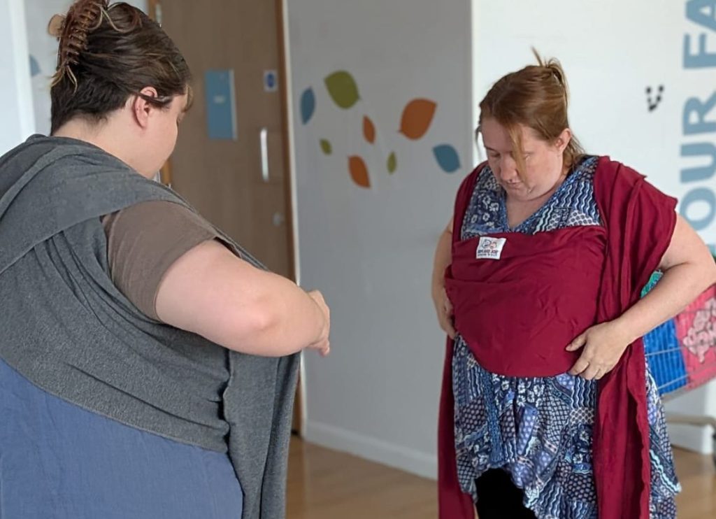 Baby Carrying Consultant Supports Parent learning to carry their baby in a library carrier at Portsmouth and Southsea Sling Library.